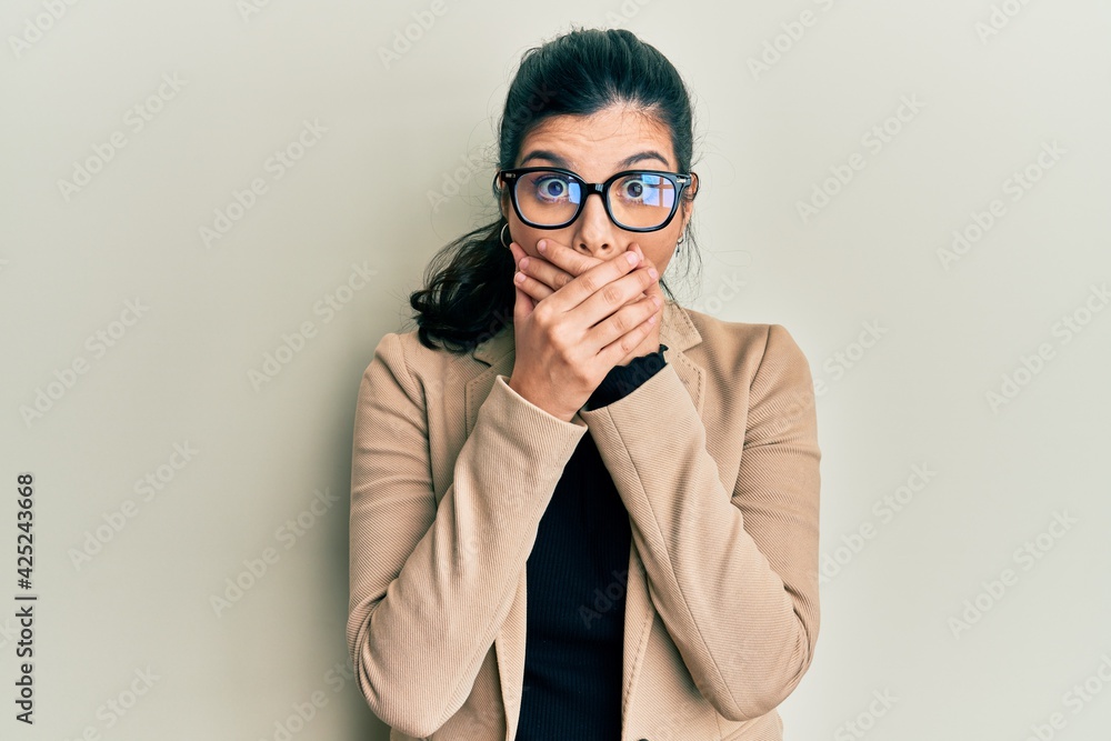 Young hispanic woman wearing business style and glasses shocked covering mouth with hands for mistake. secret concept. Young hispanic woman wearing business style and glasses shocked covering mouth with hands for mistake. secret concept.