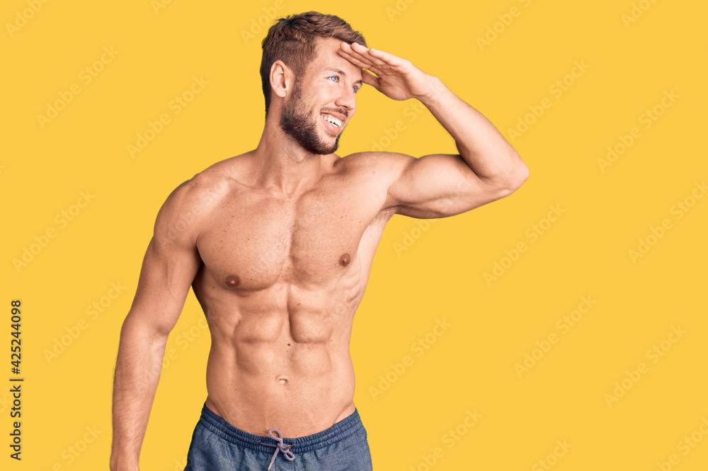 Young caucasian man standing shirtless very happy and smiling looking far away with hand over head. searching concept.