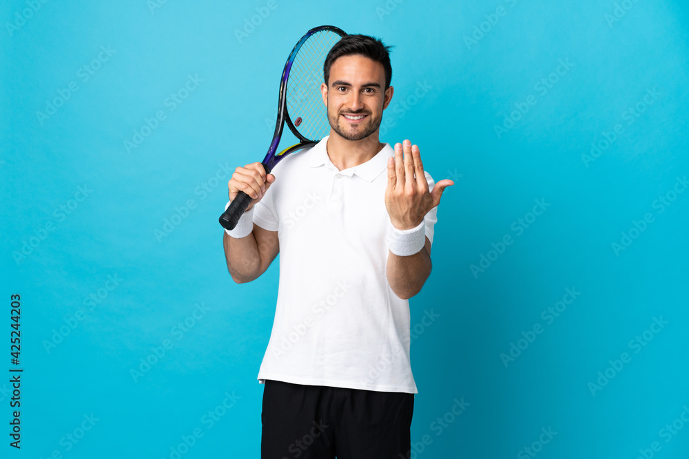 Young handsome man isolated on blue background playing tennis and doing coming gesture Young handsome man isolated on blue background playing tennis and doing coming gesture