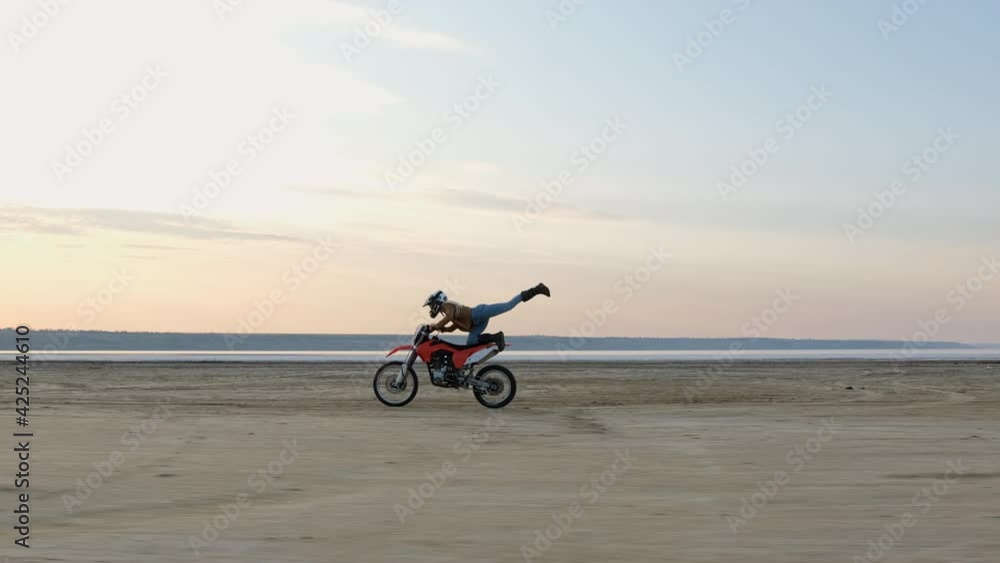 A sportswoman doing stunts on a sports bike as she rides at speed along the wide beach of the lake. A sportswoman doing stunts on a sports bike as she rides at speed along the wide beach of the lake.