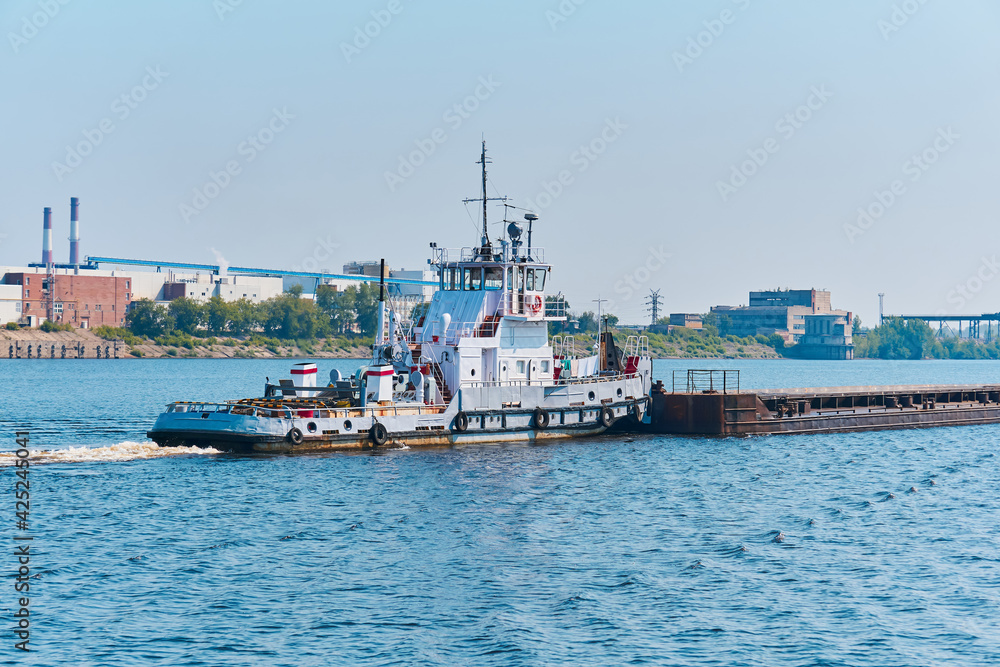 towboat pushes dry bulk cargo barge on the river in an industrial landscape