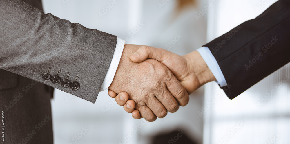 Business people in office suits standing and shaking hands, close-up. Business communication concept. Handshake and marketing