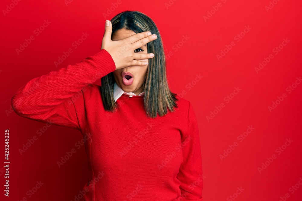 Young latin woman wearing casual clothes peeking in shock covering face and eyes with hand, looking through fingers with embarrassed expression. Young latin woman wearing casual clothes peeking in shock covering face and eyes with hand, looking through fingers with embarrassed expression.