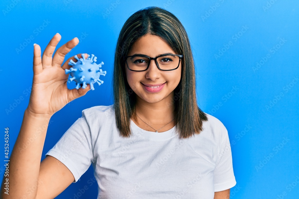 Fototapeta premium Young latin woman holding virus toy looking positive and happy standing and smiling with a confident smile showing teeth