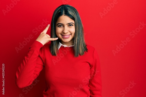 Young latin woman wearing casual clothes smiling doing phone gesture with hand and fingers like talking on the telephone. communicating concepts. © Krakenimages.com
