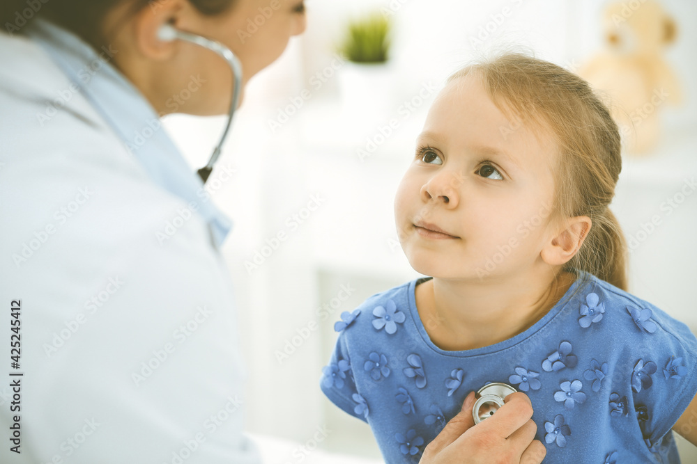 Doctor examining a child by stethoscope. Happy smiling girl patient dressed in blue dress is at usual medical inspection. Medicine concept Doctor examining a child by stethoscope. Happy smiling girl patient dressed in blue dress is at usual medical inspection. Medicine concept