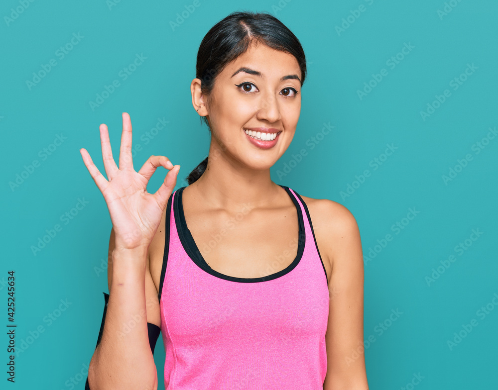 Beautiful asian young sport woman wearing sportswear and arm band smiling positive doing ok sign with hand and fingers. successful expression. Beautiful asian young sport woman wearing sportswear and arm band smiling positive doing ok sign with hand and fingers. successful expression.