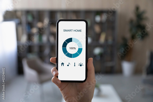 Close up of woman hold modern cellphone with smart home application on screen. African American female use smarthome system control panel on smartphone gadget. Modern technology concept.