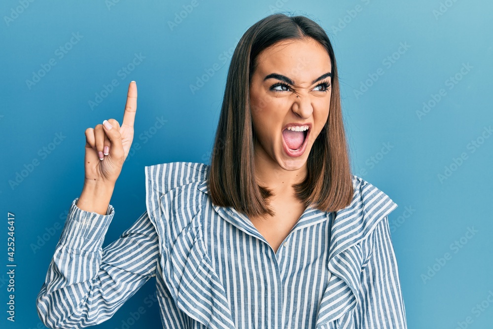 Young brunette student girl pointing up with finger angry and mad screaming frustrated and furious, shouting with anger. rage and aggressive concept. Young brunette student girl pointing up with finger angry and mad screaming frustrated and furious, shouting with anger. rage and aggressive concept.