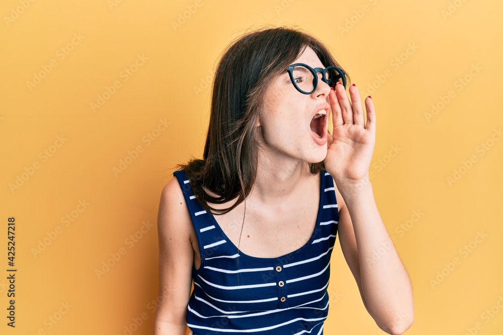 Young beautiful caucasian girl wearing casual clothes and glasses shouting and screaming loud to side with hand on mouth. communication concept. Young beautiful caucasian girl wearing casual clothes and glasses shouting and screaming loud to side with hand on mouth. communication concept.