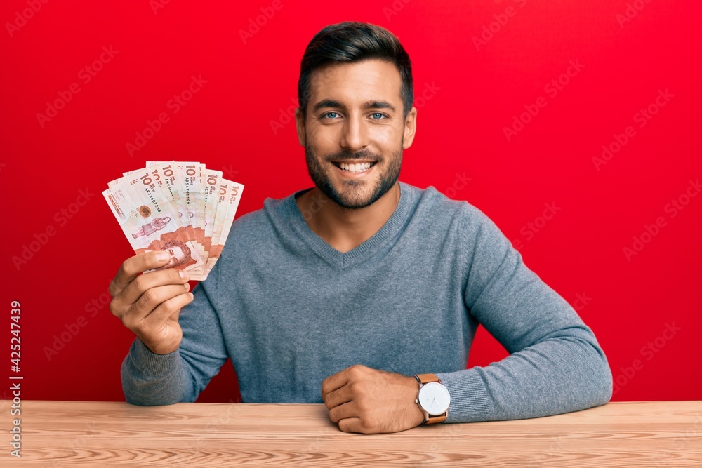 Handsome hispanic man holding colombian pesos looking positive and happy standing and smiling with a confident smile showing teeth Handsome hispanic man holding colombian pesos looking positive and happy standing and smiling with a confident smile showing teeth