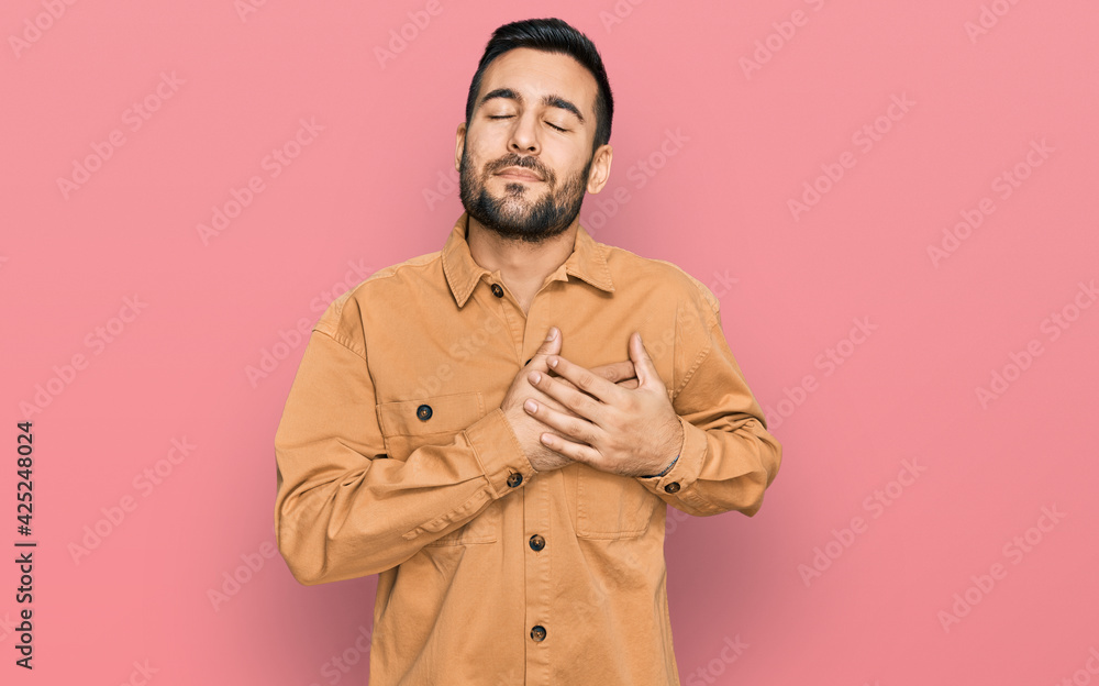 Young hispanic man wearing casual clothes smiling with hands on chest with closed eyes and grateful gesture on face. health concept. Young hispanic man wearing casual clothes smiling with hands on chest with closed eyes and grateful gesture on face. health concept.