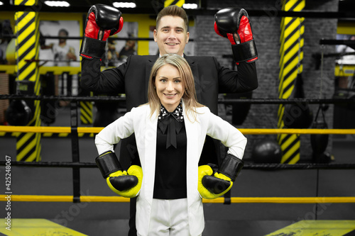 Colleagues, a man and a woman in business suits and boxing gloves in the ring.