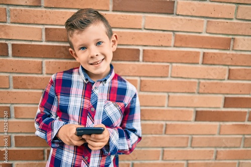 Adorable caucasian boy smiling happy using smartphone at the city.