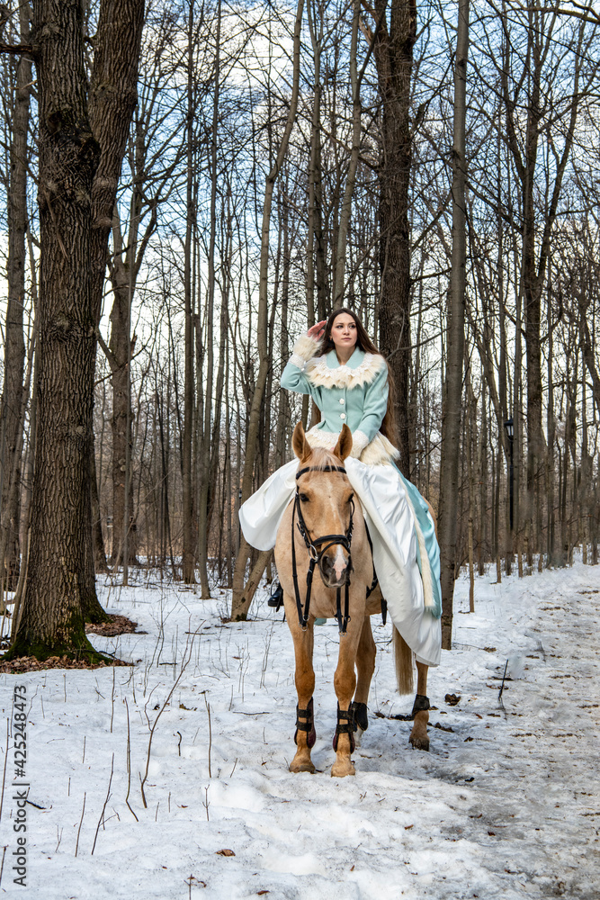 Fototapeta premium beautiful girl in a blue outfit and a light brown horse in a spring forest