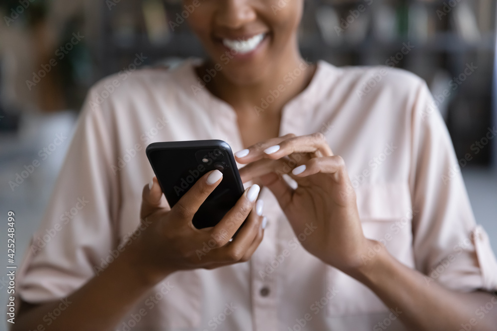 © fizkes - Crop close up of smiling biracial woman hold use modern cellphone text message online on gadget. Happy African American female browse internet or have webcam video talk on smartphone device.