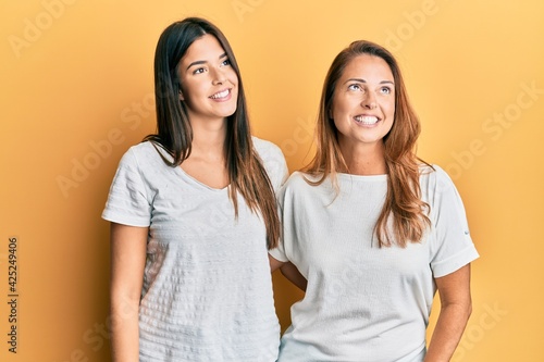 Hispanic family of mother and daughter wearing casual white tshirt smiling looking to the side and staring away thinking.