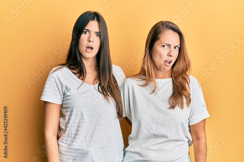 Hispanic family of mother and daughter wearing casual white tshirt in shock face, looking skeptical and sarcastic, surprised with open mouth