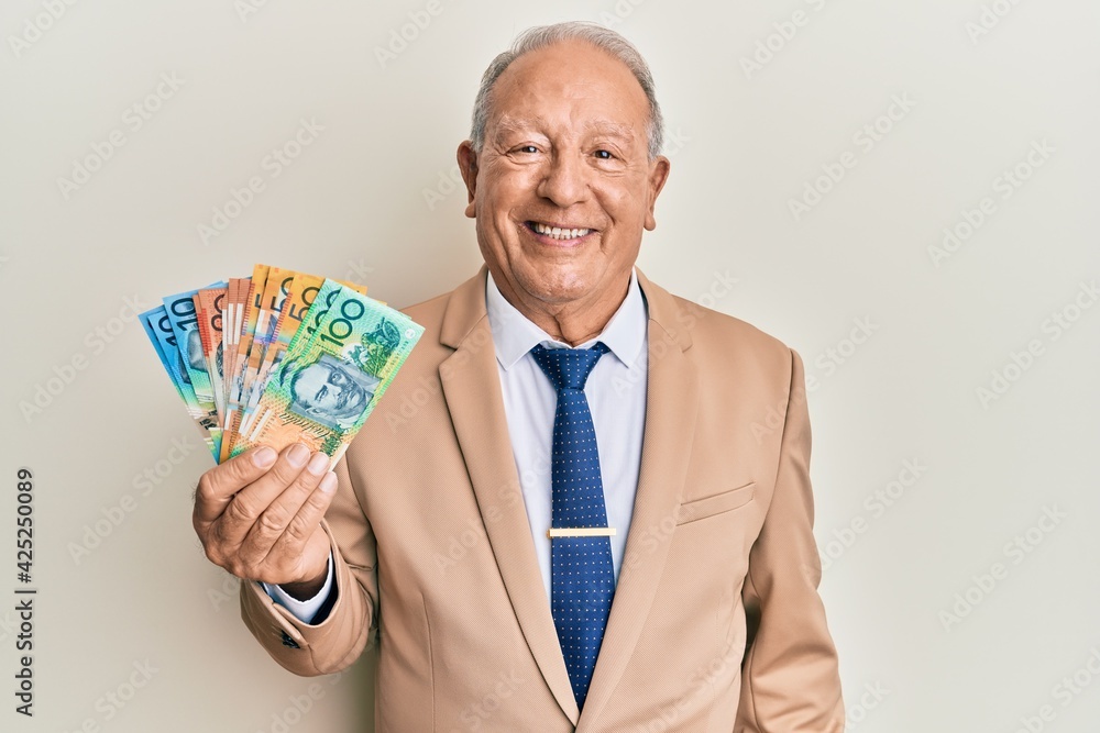 Senior caucasian man holding australian dollars looking positive and happy standing and smiling with a confident smile showing teeth Senior caucasian man holding australian dollars looking positive and happy standing and smiling with a confident smile showing teeth