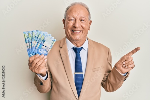 Senior caucasian man holding south african 20 rand banknotes smiling happy pointing with hand and finger to the side