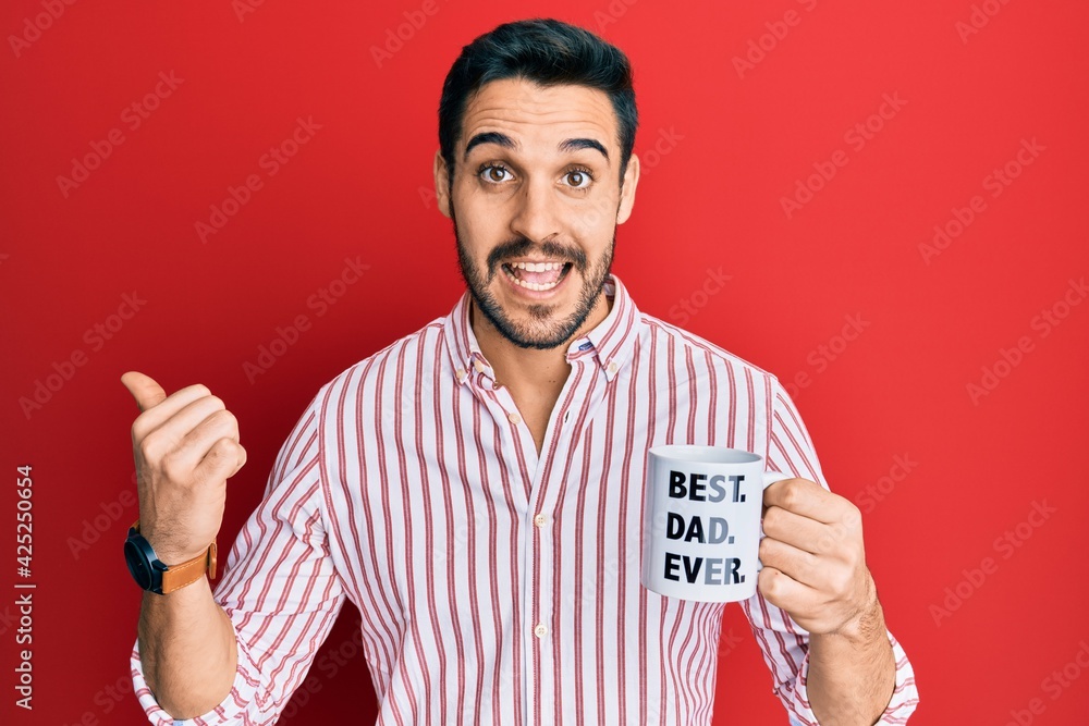 Young hispanic man drinking mug of coffe with best dad ever message pointing thumb up to the side smiling happy with open mouth Young hispanic man drinking mug of coffe with best dad ever message pointing thumb up to the side smiling happy with open mouth