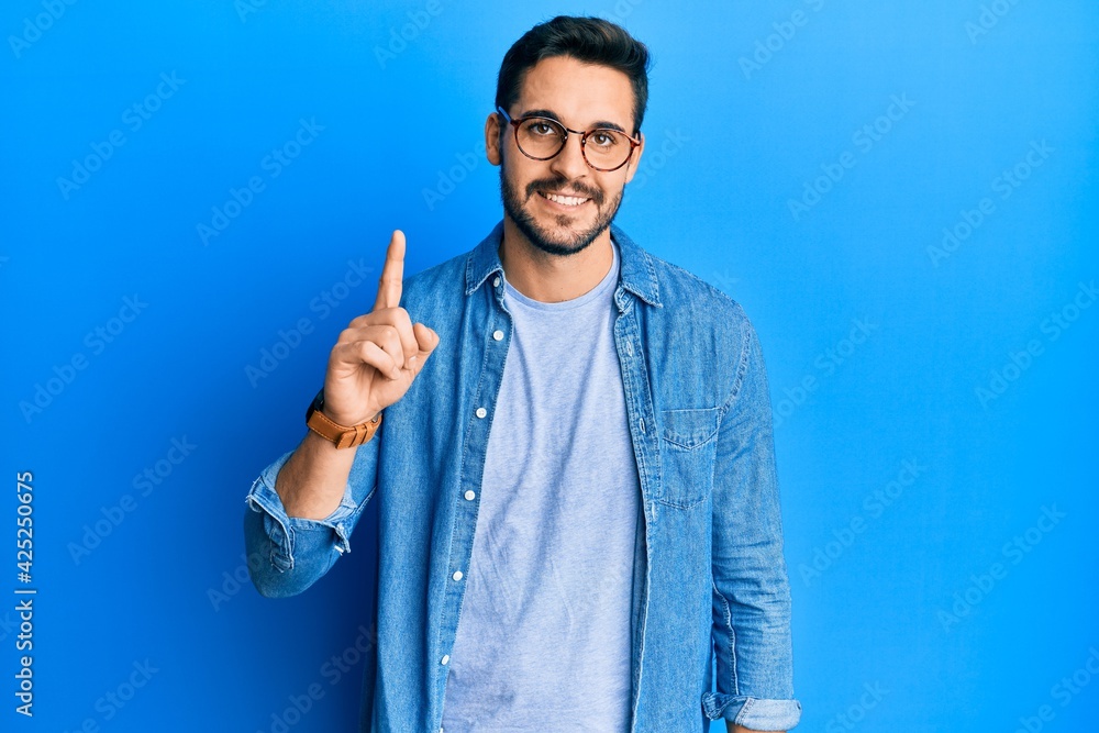 Young hispanic man wearing casual clothes and glasses smiling with an idea or question pointing finger up with happy face, number one Young hispanic man wearing casual clothes and glasses smiling with an idea or question pointing finger up with happy face, number one