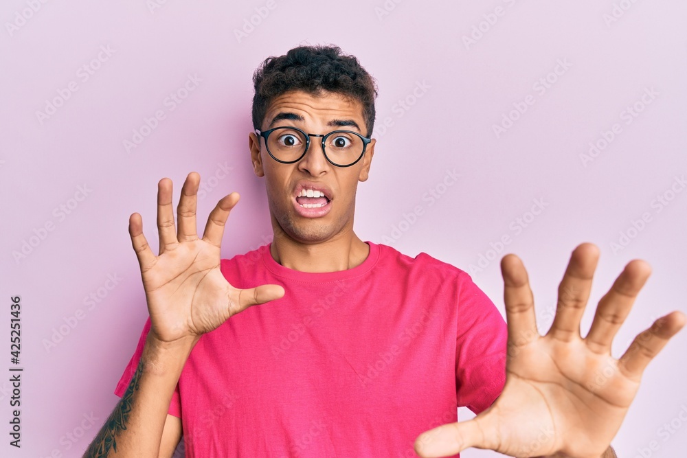 Young handsome african american man wearing glasses over pink background afraid and terrified with fear expression stop gesture with hands, shouting in shock. panic concept. Young handsome african american man wearing glasses over pink background afraid and terrified with fear expression stop gesture with hands, shouting in shock. panic concept.