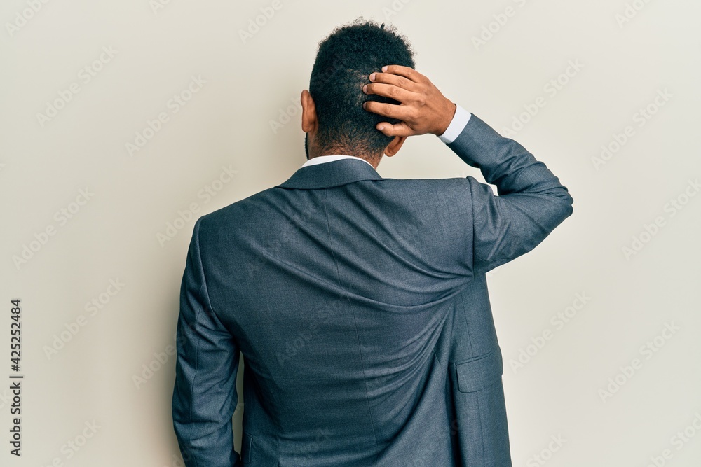 Handsome hispanic man with beard wearing business suit and tie backwards thinking about doubt with hand on head Handsome hispanic man with beard wearing business suit and tie backwards thinking about doubt with hand on head