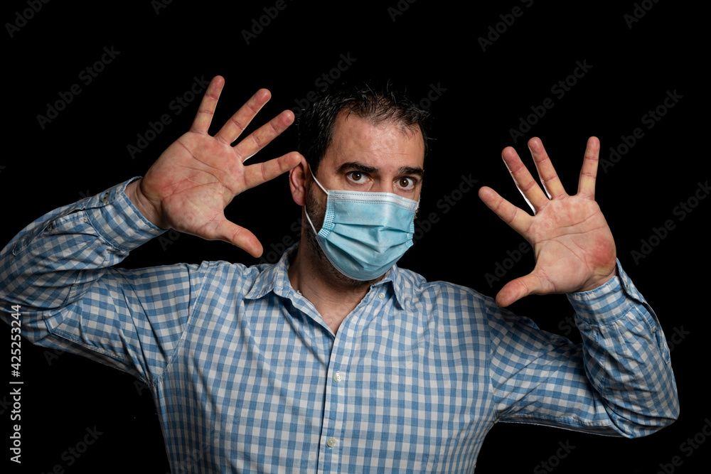 Man wearing surgical mask to protect himself from coronavirus posing with open palms in alert sign on black studio background Man wearing surgical mask to protect himself from coronavirus posing with open palms in alert sign on black studio background