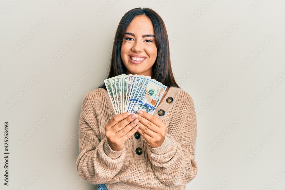 Young beautiful hispanic girl holding dollars smiling with a happy and cool smile on face. showing teeth. Young beautiful hispanic girl holding dollars smiling with a happy and cool smile on face. showing teeth.