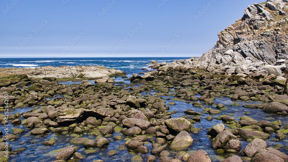Orilla en bajamar (low tide) de un acantilado con guijarros y agua azul en las Islas Cies, Galicia, España. Orilla en bajamar (low tide) de un acantilado con guijarros y agua azul en las Islas Cies, Galicia, España.