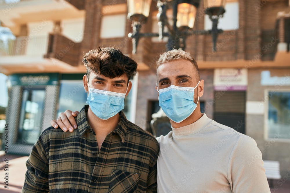 Young gay couple wearing medical mask hugging at the city.