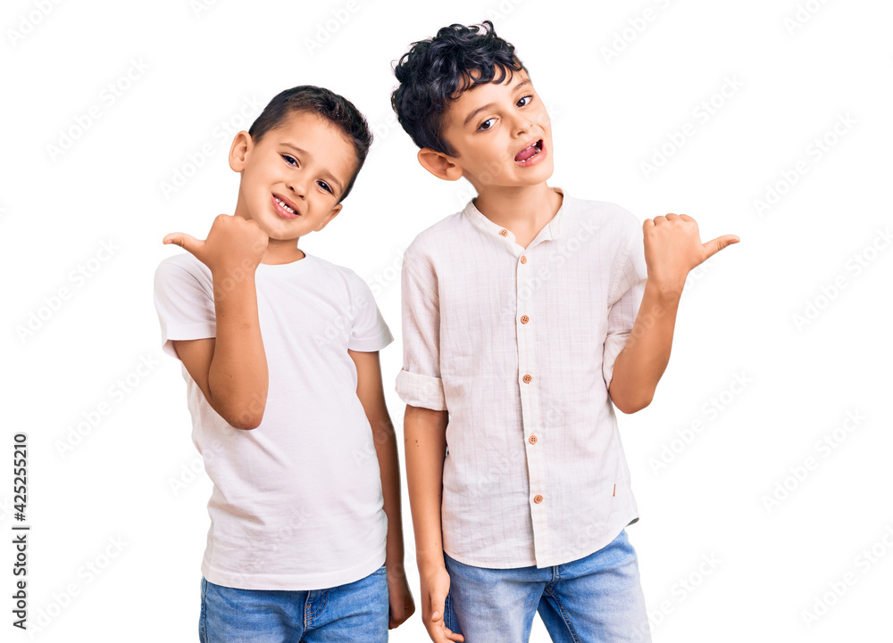 Couple of little brothers together wearing casual clothes smiling with happy face looking and pointing to the side with thumb up. Couple of little brothers together wearing casual clothes smiling with happy face looking and pointing to the side with thumb up.