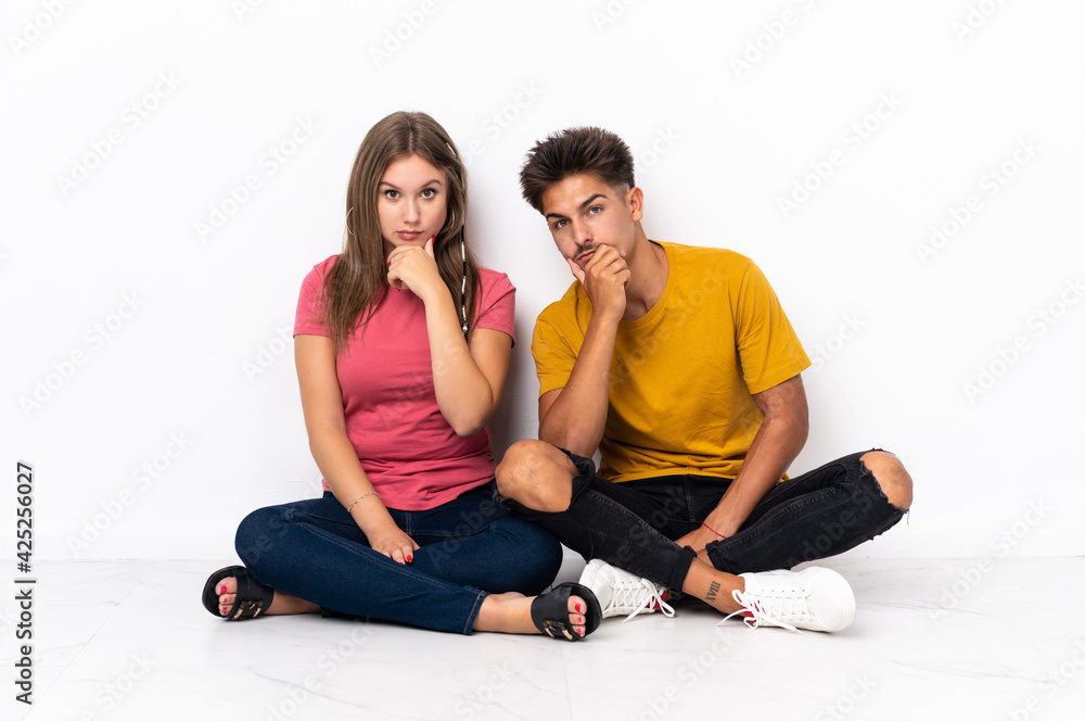 Young couple sitting on the floor isolated on white background thinking Young couple sitting on the floor isolated on white background thinking