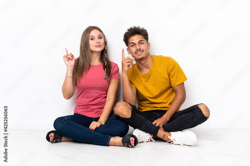 Fototapeta premium Young couple sitting on the floor isolated on white background pointing up a great idea