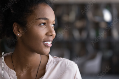 Close up of happy millennial African American woman look in distance thinking or dreaming. Smiling young biracial female imagine or visualize future success or opportunities. Vision, hope concept.