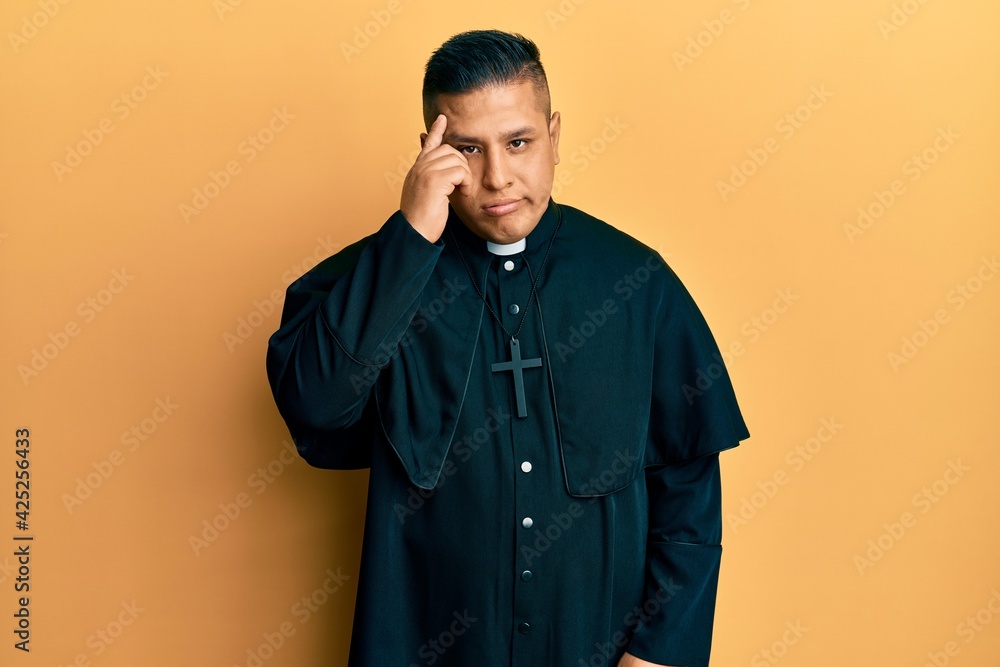 Young latin priest man standing over yellow background worried and stressed about a problem with hand on forehead, nervous and anxious for crisis Young latin priest man standing over yellow background worried and stressed about a problem with hand on forehead, nervous and anxious for crisis