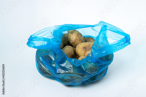 Plastic bag with potatoes on a white background. Blue package with potatoes on a light background. Products in the bag