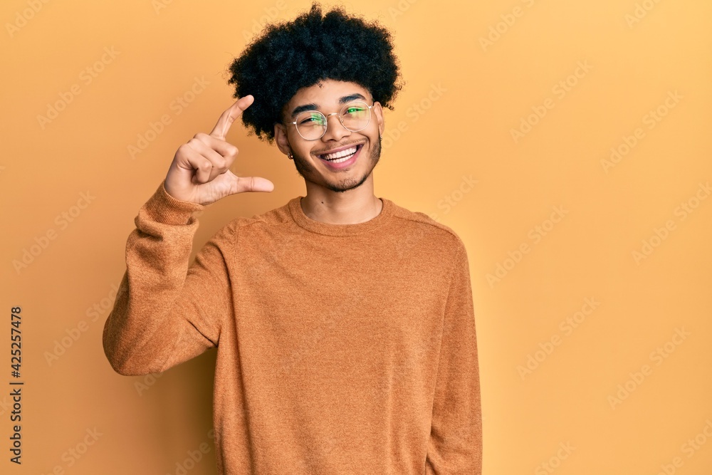 Young african american man with afro hair wearing casual winter sweater smiling and confident gesturing with hand doing small size sign with fingers looking and the camera. measure concept. Young african american man with afro hair wearing casual winter sweater smiling and confident gesturing with hand doing small size sign with fingers looking and the camera. measure concept.