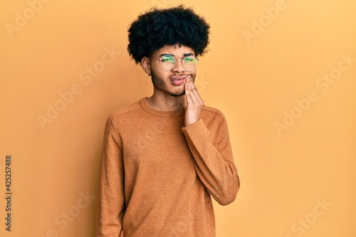 Young african american man with afro hair wearing casual winter sweater touching mouth with hand with painful expression because of toothache or dental illness on teeth. dentist © Krakenimages.com
