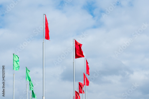 Flagpoles with red and green flags on cloudy sky background