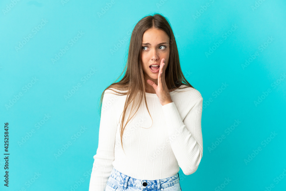 Young woman over isolated blue background whispering something with surprise gesture while looking to the side Young woman over isolated blue background whispering something with surprise gesture while looking to the side