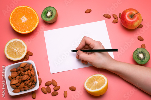 Creative layout made of various fruits and nuts with white paper sheet. Flat lay, pink background. Free space for text. Healthy food concept. Orange, lemon, kiwi, apple, nuts. High resolution product. photo