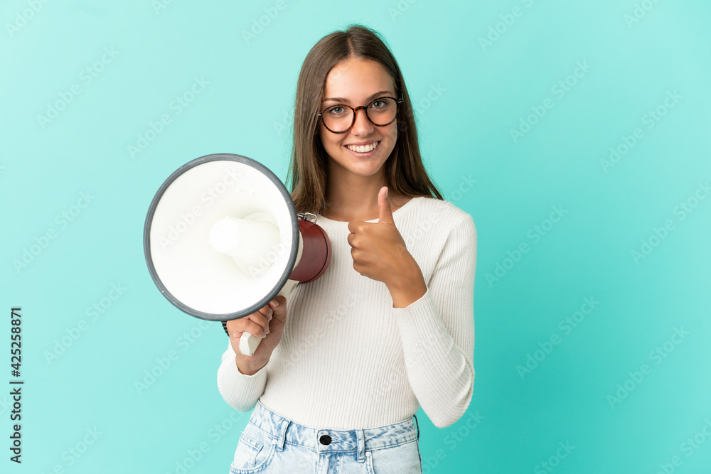 Young woman over isolated blue background holding a megaphone with thumb up Young woman over isolated blue background holding a megaphone with thumb up