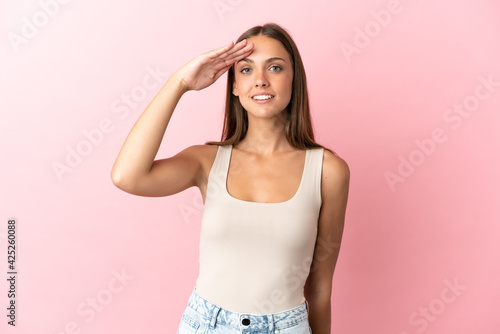 Young woman over isolated pink background saluting with hand with happy expression © luismolinero