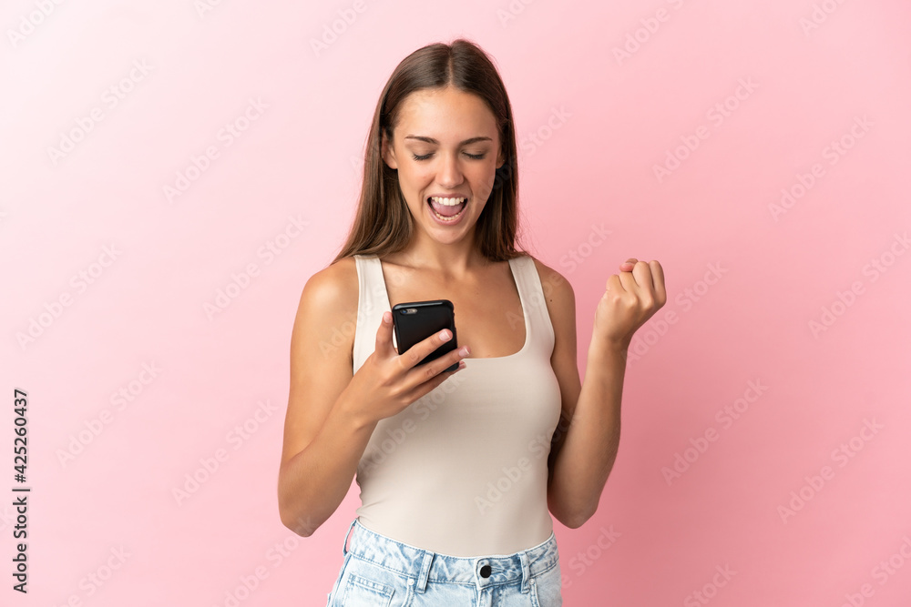 Young woman over isolated pink background with phone in victory position Young woman over isolated pink background with phone in victory position