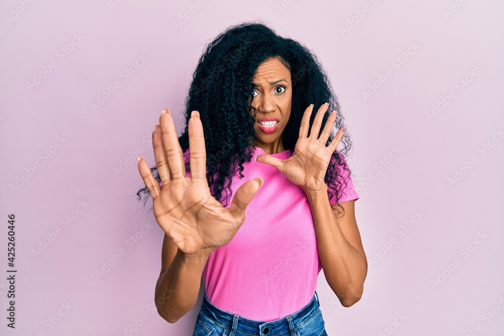 Middle age african american woman wearing casual clothes afraid and terrified with fear expression stop gesture with hands, shouting in shock. panic concept. Middle age african american woman wearing casual clothes afraid and terrified with fear expression stop gesture with hands, shouting in shock. panic concept.