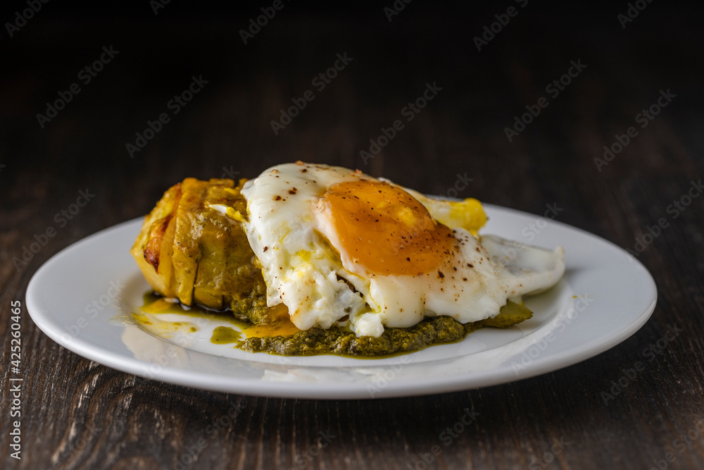 Baked potato with fried egg in white plate, close up