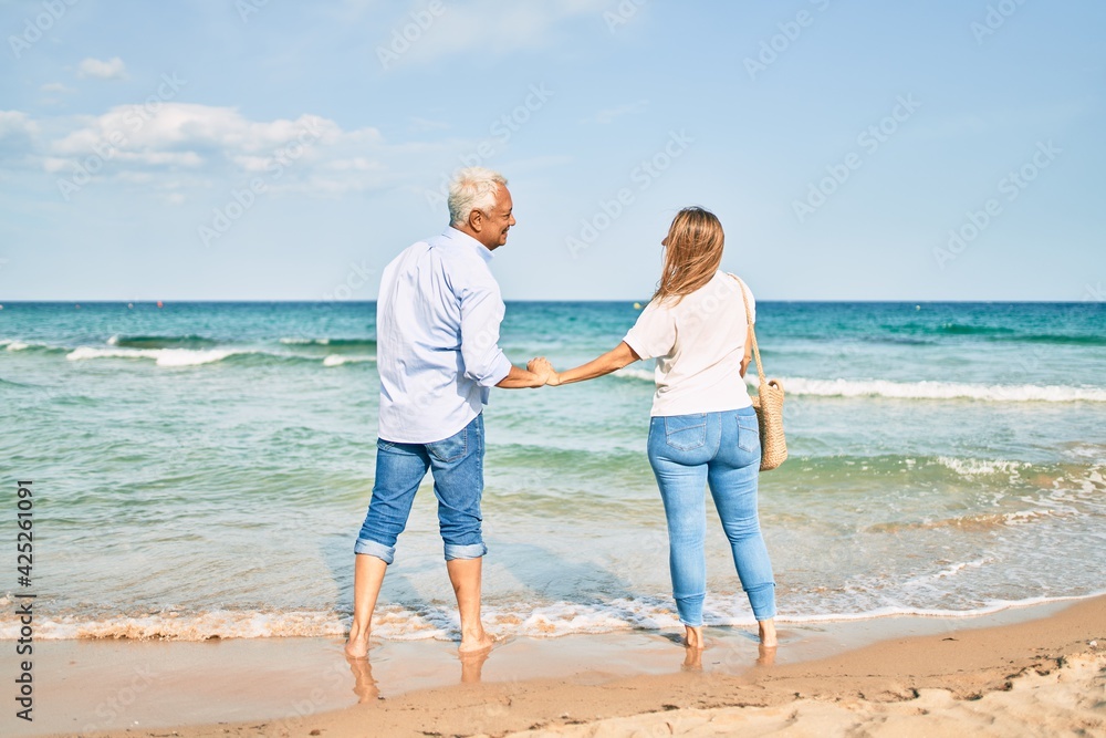 Middle age hispanic couple smiling happy looking at each other face at the beach.