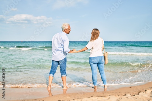 Middle age hispanic couple smiling happy looking at each other face at the beach.